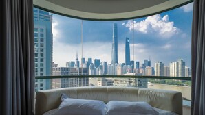 Una camera d'albergo con un letto grande, vista sullo skyline cittadino e balcone in vetro.
