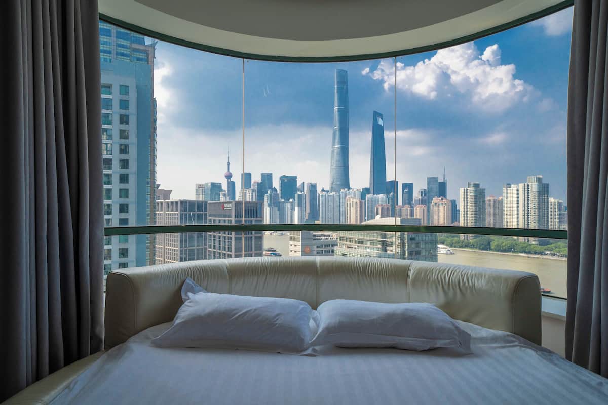 Une chambre d’hôtel avec un grand lit, une vue sur les toits de la ville et un balcon en verre.