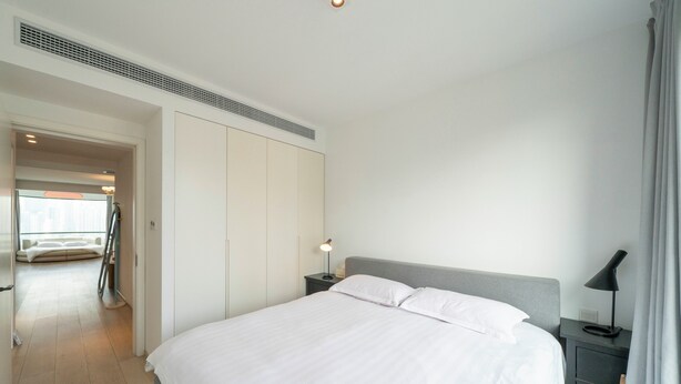 Een moderne hotelkamer met een groot bed, een nachtkastje met lamp, een kledingkast en uitzicht op een balkon.