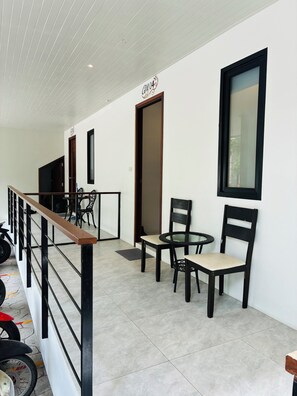 A hallway with a wooden railing, a table with chairs, and a motorcycle parked to the left. - Hillside Haven-Luxury Room (Koh Samui)