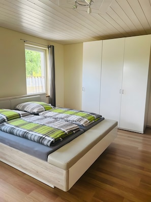 Un dormitorio con cama, armario, ventana con cortinas y ventilador de techo.