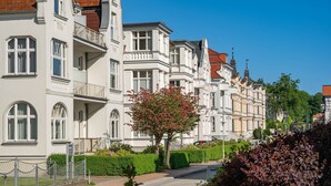 A row of white buildings with balconies, a tree with pink flowers, and a clear blue sky.