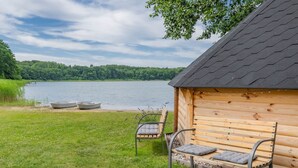 A wooden cabin with a bench and two boats by a lake.