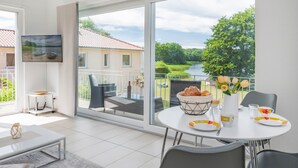 Habitación moderna con balcón, una mesa de comedor dispuesta con platos y vasos, y vistas a un río y vegetación.