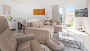 Una sala de estar moderna con un sofá color beige, una mesa de centro y un televisor montado en la pared.