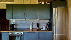 A modern kitchen with dark cabinets, a stainless steel refrigerator, a built-in oven, and a wooden countertop.