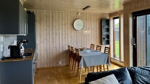 A modern kitchen with dark cabinets, a wooden dining area with a table and chairs, and a large window with a view of greenery.