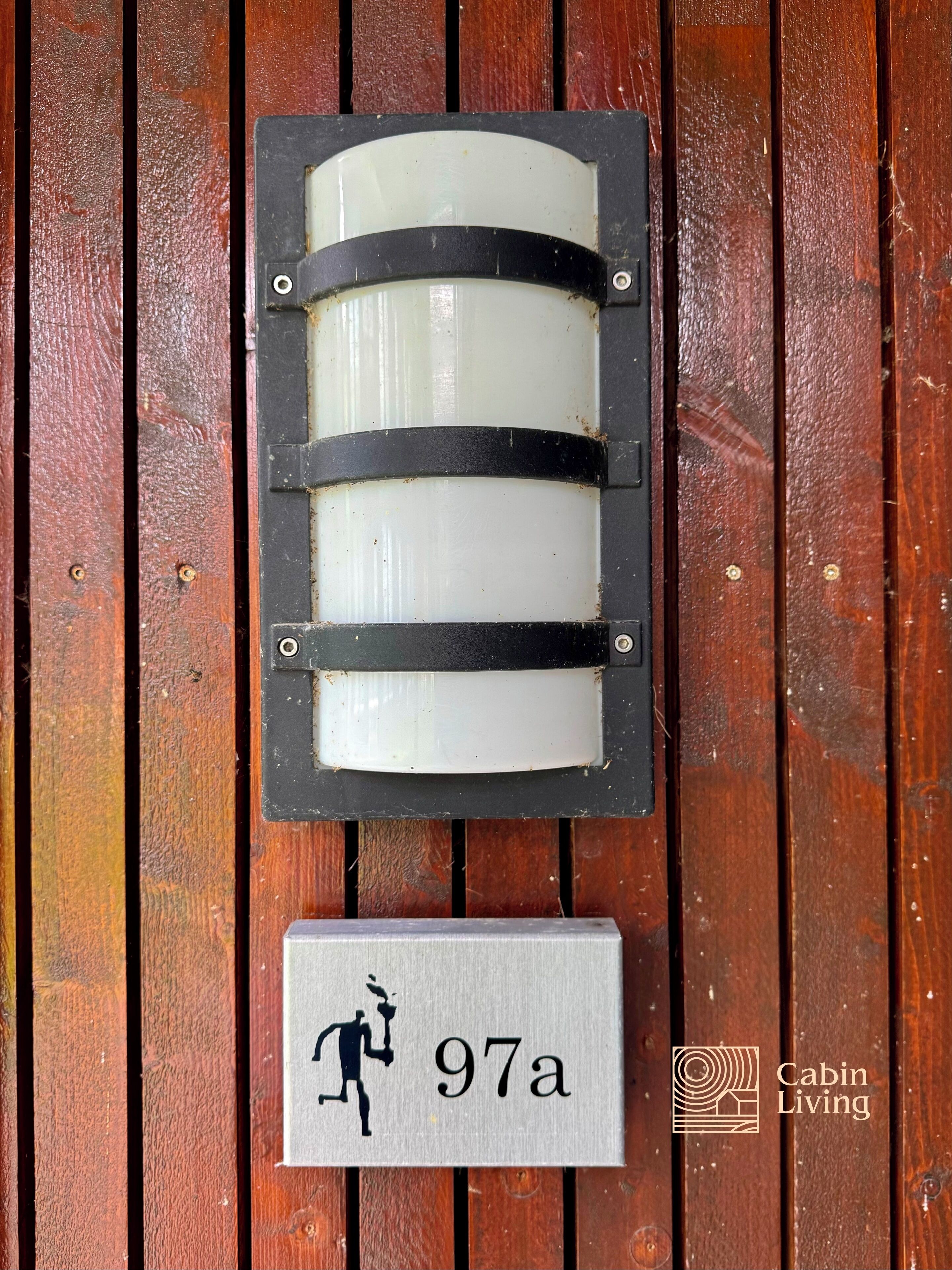 Une porte de style chalet, avec une plaque portant le numéro « 97a » et la silhouette d’une personne tenant une torche.