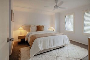 Ein Schlafzimmer mit einem Bett, Nachttischlampen, einem Deckenventilator und einem Fenster mit Jalousien.