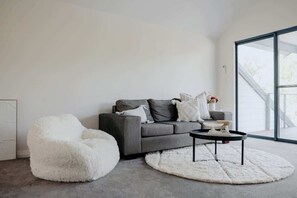 Ein modernes Wohnzimmer mit einem grauen Sofa, einem weißen, flauschigen Sessel und einem runden Couchtisch.