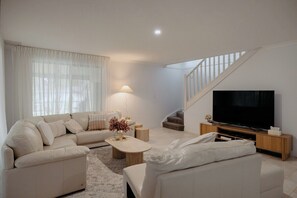 Ein modernes Wohnzimmer mit einem Ecksofa, einem Couchtisch, einem Flachbildfernseher und einer Treppe.