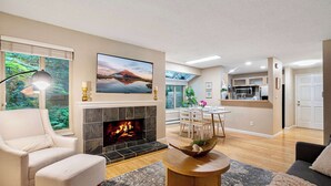 Ein modernes Wohnzimmer mit Kamin, einem Essbereich mit Tisch und Stühlen sowie einer Küche im Hintergrund.