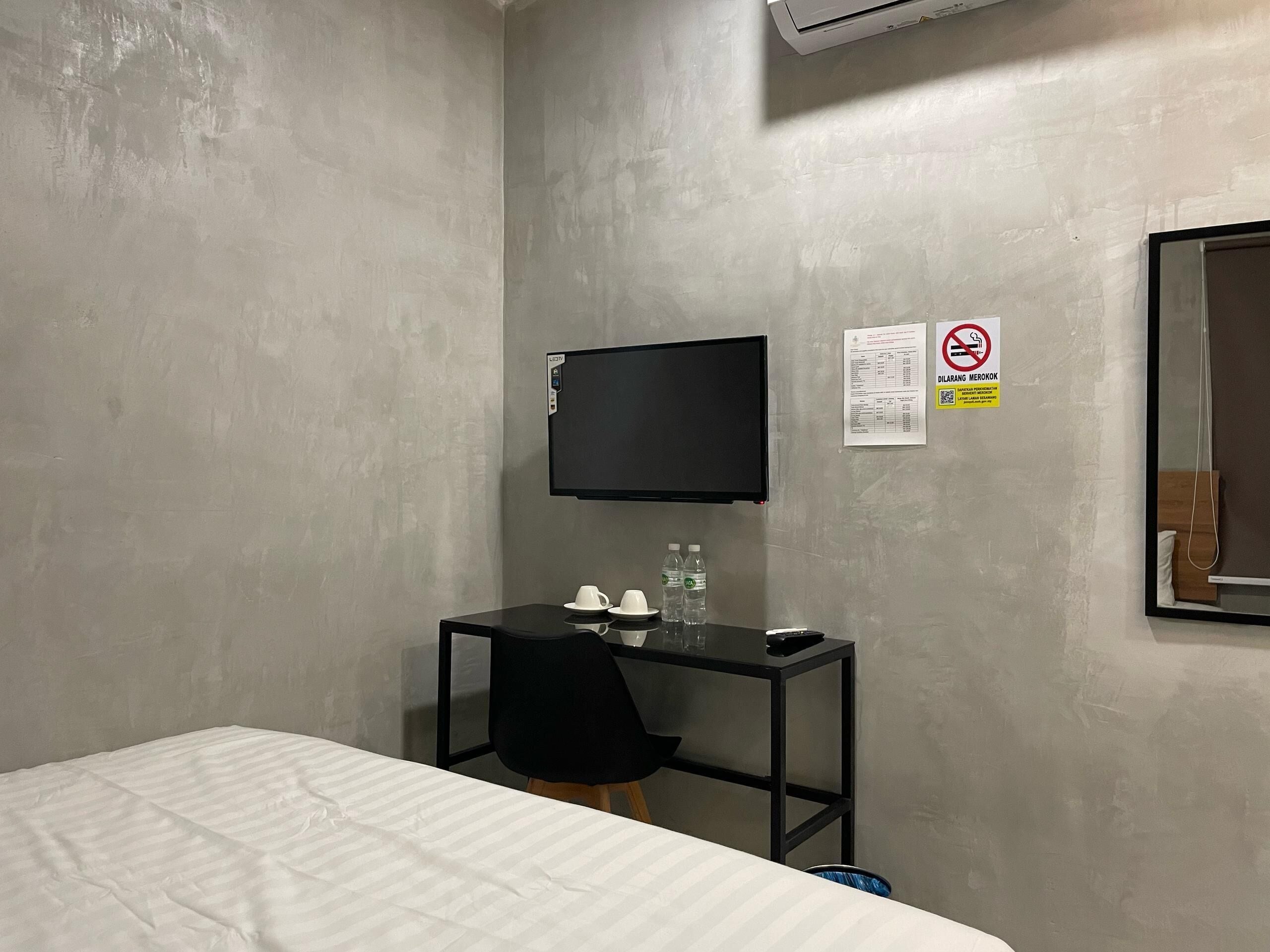 Ein Hotelzimmer mit Bett, Schreibtisch mit Stuhl, Flachbildfernseher und einer Wasserflasche.