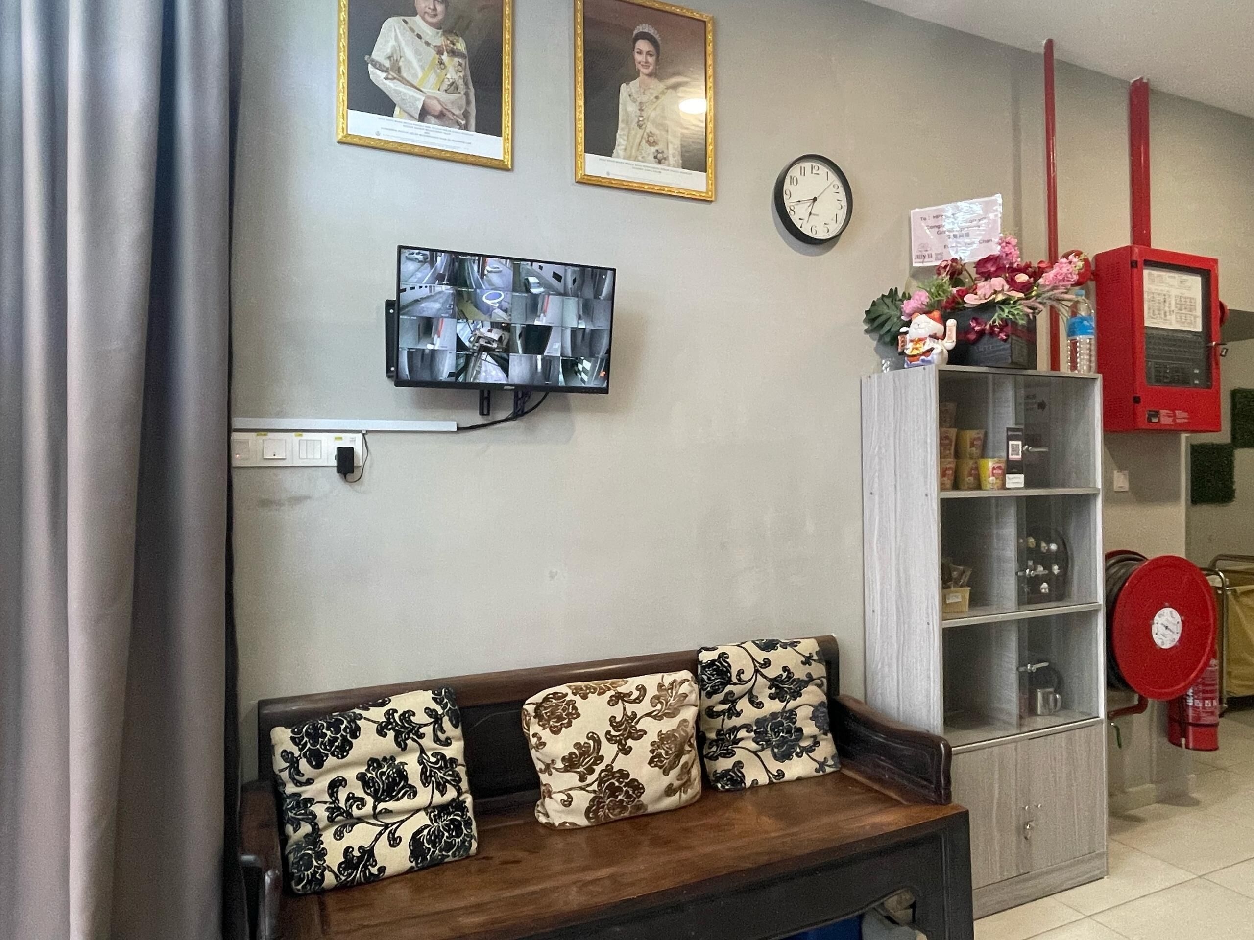 Una sala de estar con un sofá, un televisor montado en la pared, un reloj y una estantería con varios objetos.