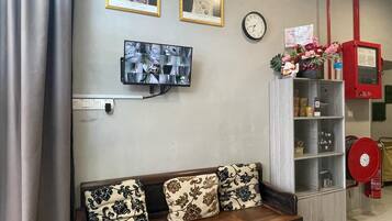 Una sala de estar con un sofá, un televisor montado en la pared, un reloj y una estantería con varios objetos.