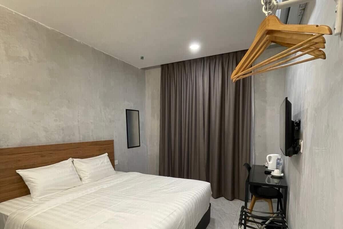 A hotel room with a bed, a small table with a kettle, and a chair.