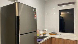 A kitchen with a stainless steel refrigerator, a wooden cabinet, a window, and a countertop with various items. - HPY Hotel (Ipoh)