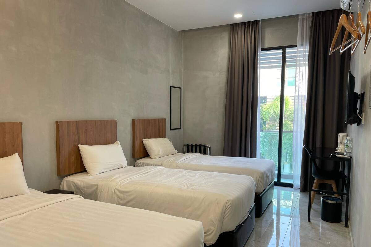A hotel room with two beds, a small table with a coffee maker, and a view of greenery outside.