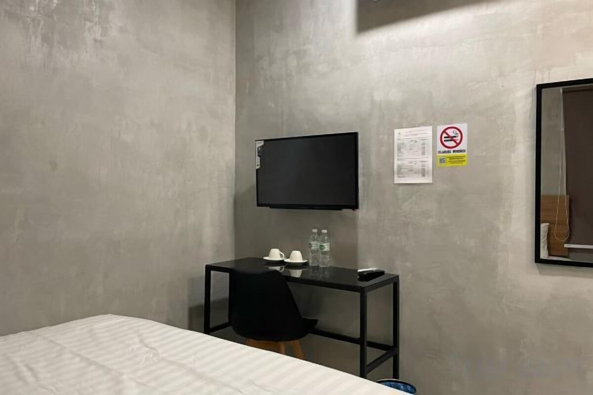 A hotel room with a bed, a desk with a chair, a flat-screen TV, and a window.