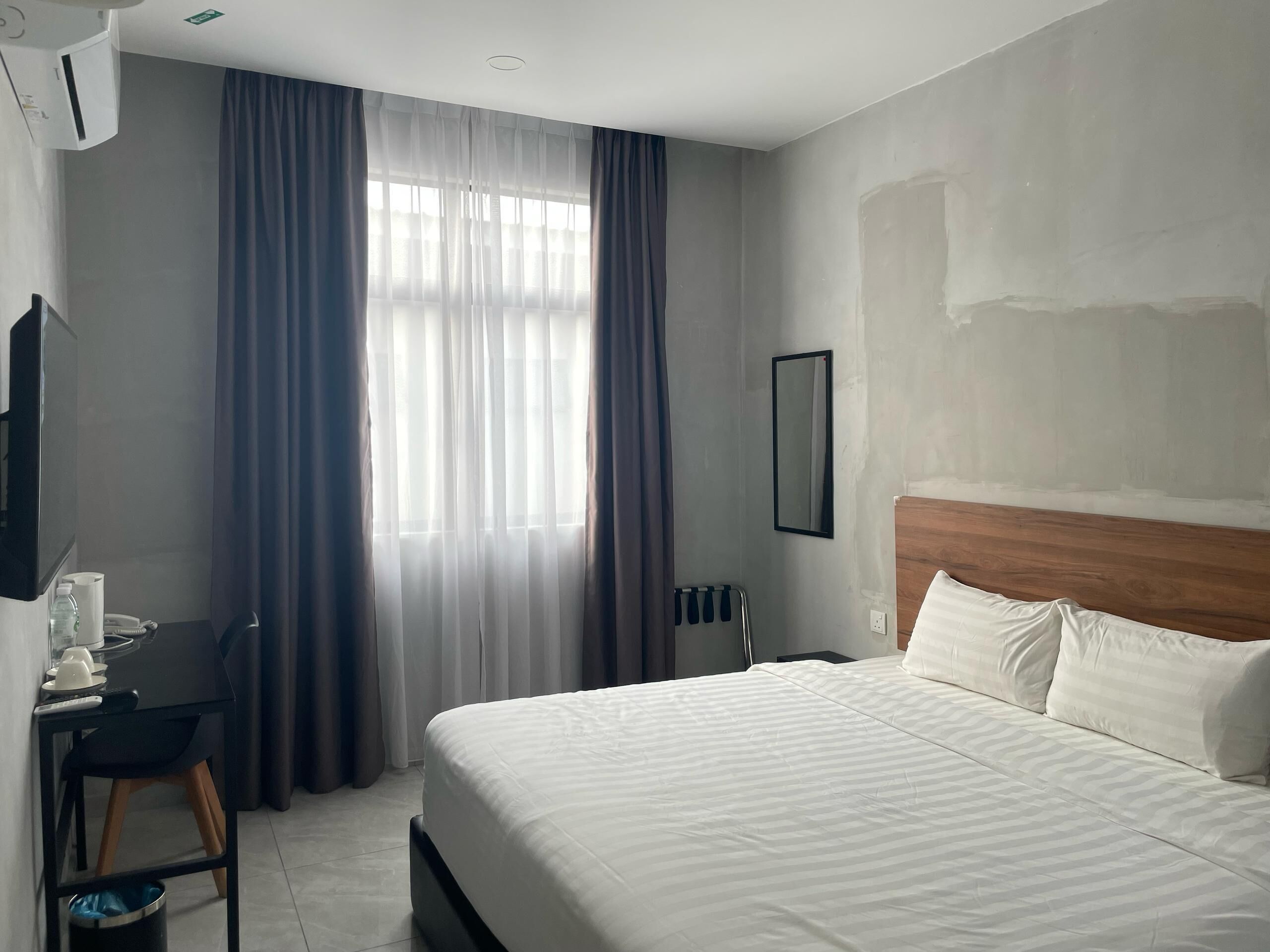 A hotel room with a bed, a desk, a chair, a mirror, and a window with curtains.