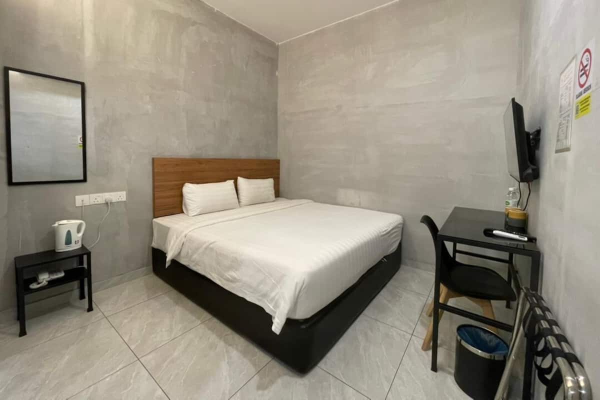 A hotel room with a bed, a small table, a chair, a kettle, and a TV.