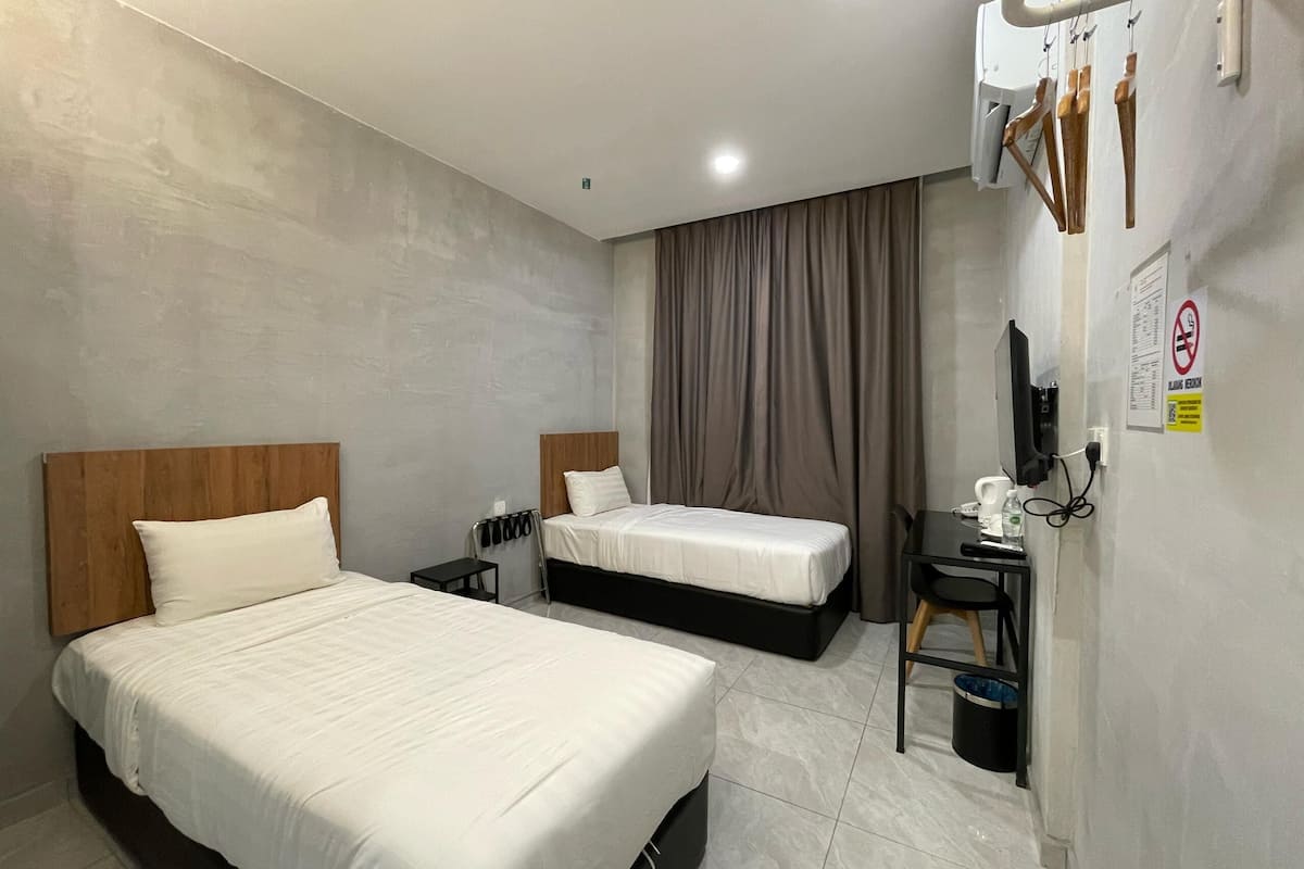 A hotel room with two beds, a desk, a chair, a TV, and a bathroom.