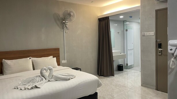 A hotel room with a large bed, a bedside table, a wall-mounted fan, a bathroom visible through an open door, and a telephone. - HPY Hotel (Ipoh)