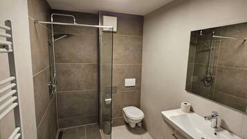 Un baño moderno con cabina de ducha de vidrio, inodoro, lavabo con espejo y perchero para toallas.