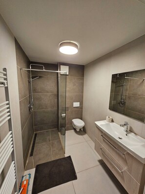 A modern bathroom with a glass shower enclosure, a toilet, a sink with a mirror, and a towel rack. - Apartments Skyreach (Essen)