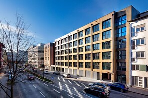 Un edificio moderno de varios pisos con una cuadrícula de ventanas, un estacionamiento con coches y un cielo despejado.