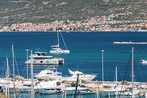 Un puerto deportivo con varios yates amarrados, un pueblo costero al fondo y un mar azul y despejado.