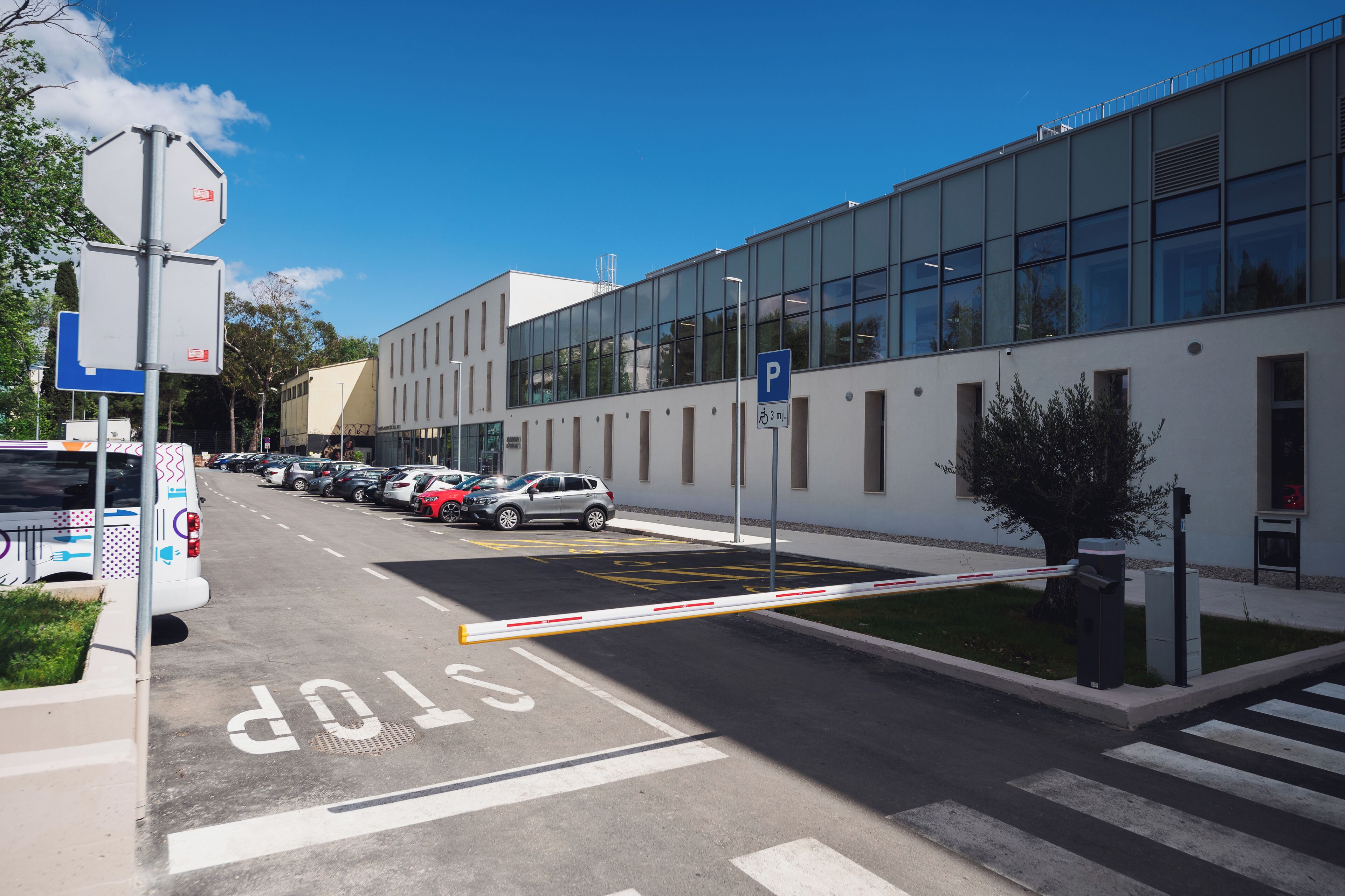 A parking lot with a gated entrance, a stop sign, and a building with large windows.