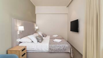 Una habitación de hotel moderna con una cama grande, dos mesitas de noche, un televisor y una ventana con cortinas.