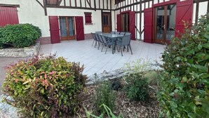 Une cour avec une table et des chaises, entourée d’un jardin où poussent différentes plantes et bordée d’un mur de pierre.