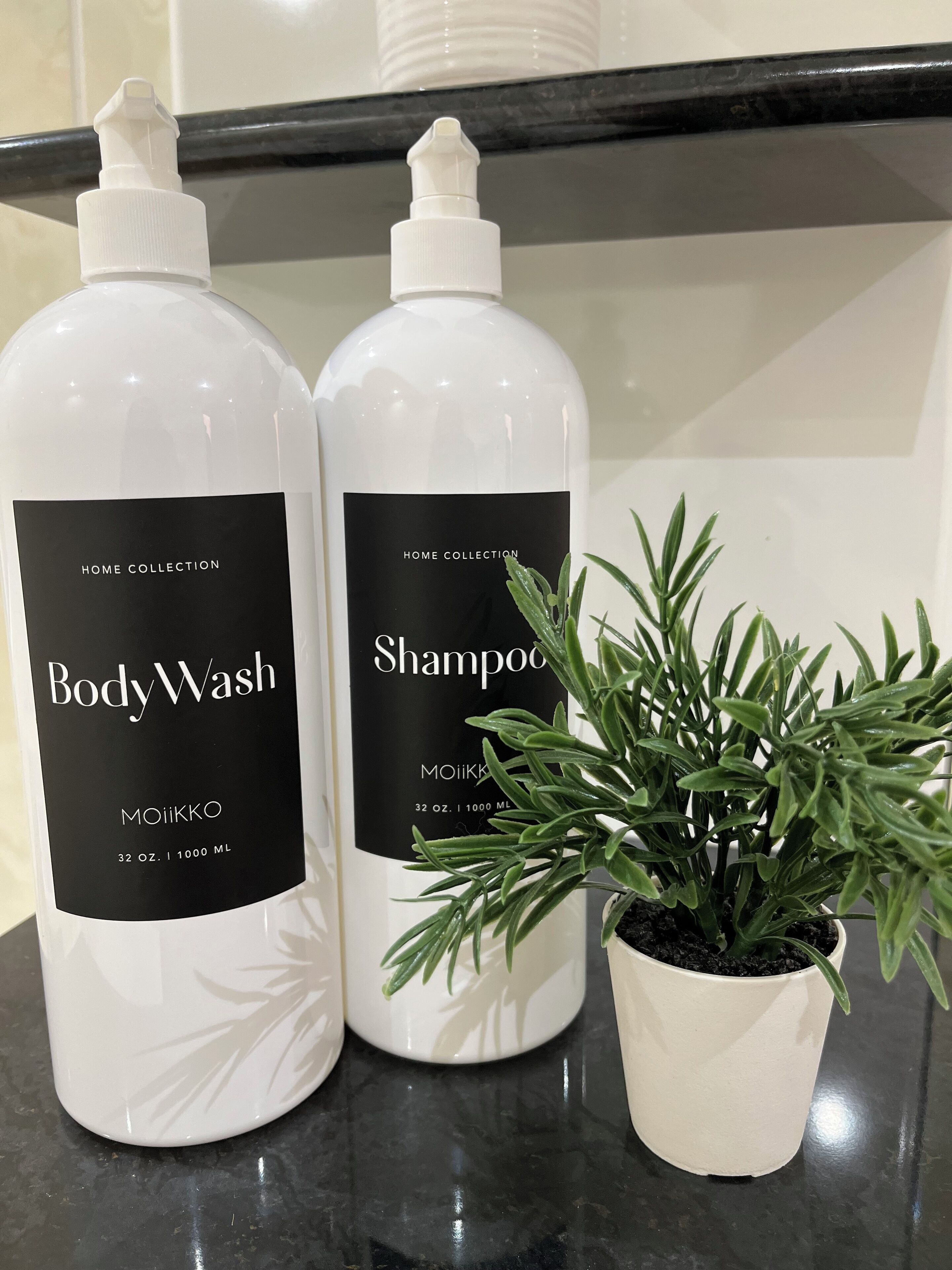 Deux flacons de gel douche et de shampoing de la gamme Home Collection, ainsi qu’une plante en pot posée sur un comptoir.