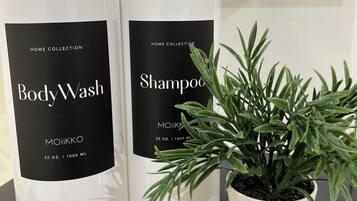 Deux flacons de gel douche et de shampoing de la gamme Home Collection, ainsi qu’une plante en pot posée sur un comptoir.