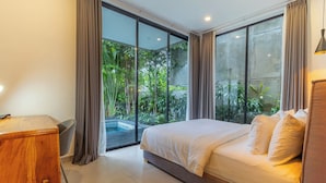 Una camera da letto con un letto, una scrivania e vista sul verde attraverso ampie finestre.