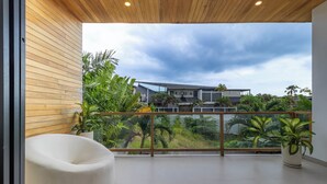 Un balcone con una poltrona sacco bianca, piante in vaso e vista su una casa moderna e vegetazione.