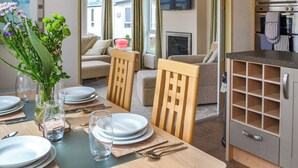 A dining area with a table set for two, a vase with flowers, and a kitchen with appliances. - 2 bedroom accommodation in Patrington Haven (Patrington Haven)