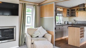 A modern living room with a sofa and ottoman, a fireplace, and a kitchen with wooden cabinets and a stove. - 2 bedroom accommodation in Patrington Haven (Patrington Haven)