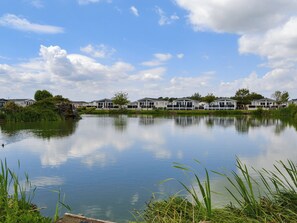 Un lago tranquilo con una hilera de cabañas blancas, una cascada pequeña y abundante vegetación.
