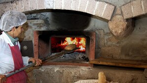A person in a hairnet and apron operating a brick oven pizza oven. - Farmhouse nestled in a cork oak forest with boungalows.  Pets allowed (Ulà Tirso)