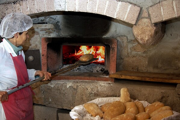 A person in a hairnet and apron operating a brick oven pizza oven. - Farmhouse nestled in a cork oak forest with boungalows.  Pets allowed (Ulà Tirso)