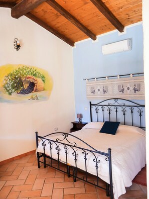 A bedroom with a bed, a nightstand, a wall-mounted air conditioner, and a decorative wall hanging. - Farmhouse nestled in a cork oak forest with boungalows.  Pets allowed (Ulà Tirso)