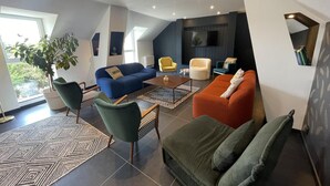 Un saló modern amb un sofà blau, un sofà taronja i una butaca verda. Hi ha una taula de centre i un televisor penjat a la paret.
