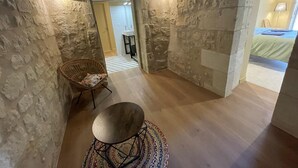Una habitació amb parets de pedra, un sòl de fusta, una taula rodona de metall i una cadira de vimet.
