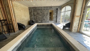 Una piscina interior rectangular amb parets de pedra i estructura de sostre de fusta.