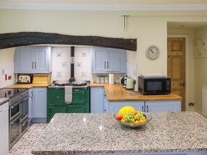 A kitchen with a granite countertop, a green stove, a microwave, and a bowl of fruit. - Hafod Grove - UKC6955 (Moylegrove, near Ceibwr Bay)