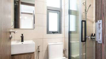 A modern bathroom with a wooden vanity, a toilet, a glass shower enclosure, and a window.