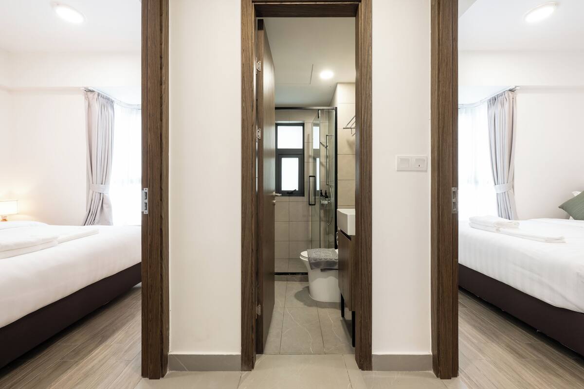 Habitación de hotel con una puerta de madera que da a un baño, una cama y un ventanal pequeño.